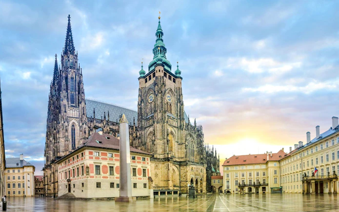 Prague Castle exterior with St. Vitus Cathedral spires at sunrise.