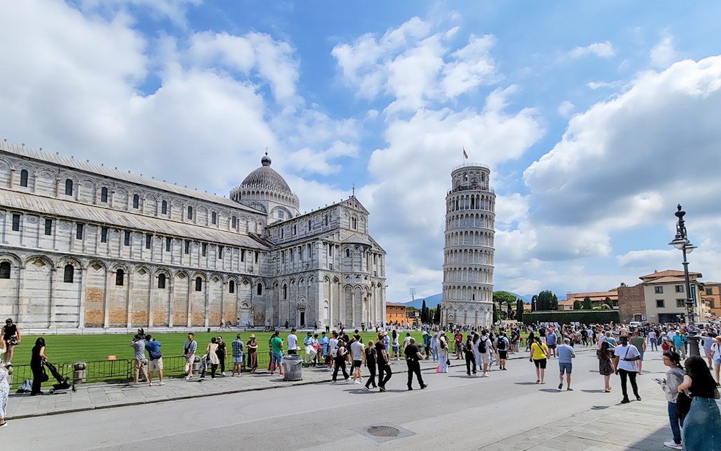 Tourists at the Square of Miracles with Pisa Cathedral and Leaning Tower, Italy.
