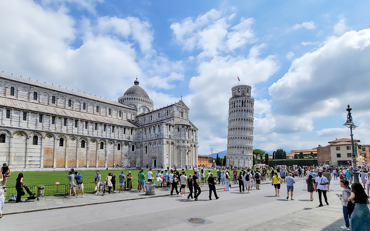 Tourists at the Square of Miracles with Pisa Cathedral and Leaning Tower, Italy.