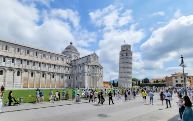 Tourists at the Square of Miracles with Pisa Cathedral and Leaning Tower, Italy.