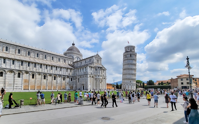 Tourists at the Square of Miracles with Pisa Cathedral and Leaning Tower, Italy.