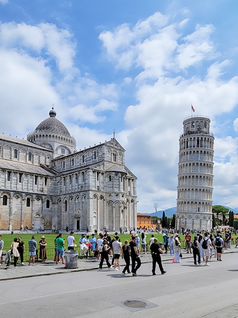 Tourists at the Square of Miracles with Pisa Cathedral and Leaning Tower, Italy.