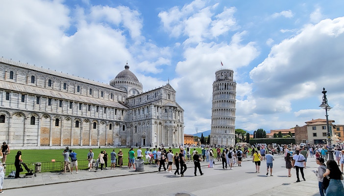 Tourists at the Square of Miracles with Pisa Cathedral and Leaning Tower, Italy.