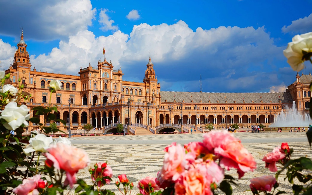 Plaza de España in Seville, Spain with vibrant flowers and fountain in foreground.