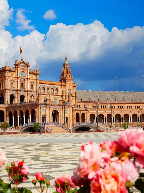 Plaza de España in Seville, Spain with vibrant flowers and fountain in foreground.