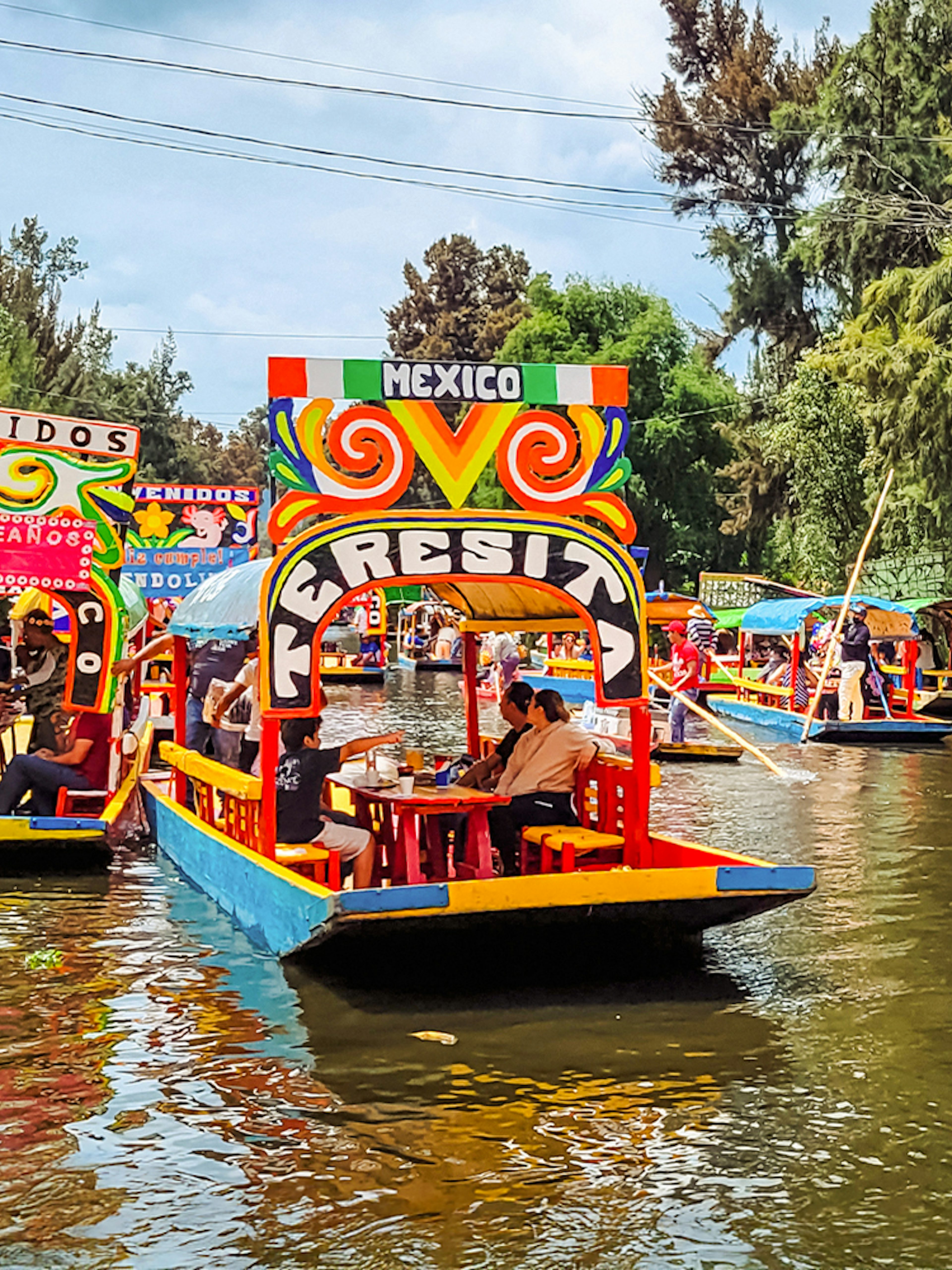 Colorful trajineras on Xochimilco canals, Mexico, with people enjoying a boat tour.
