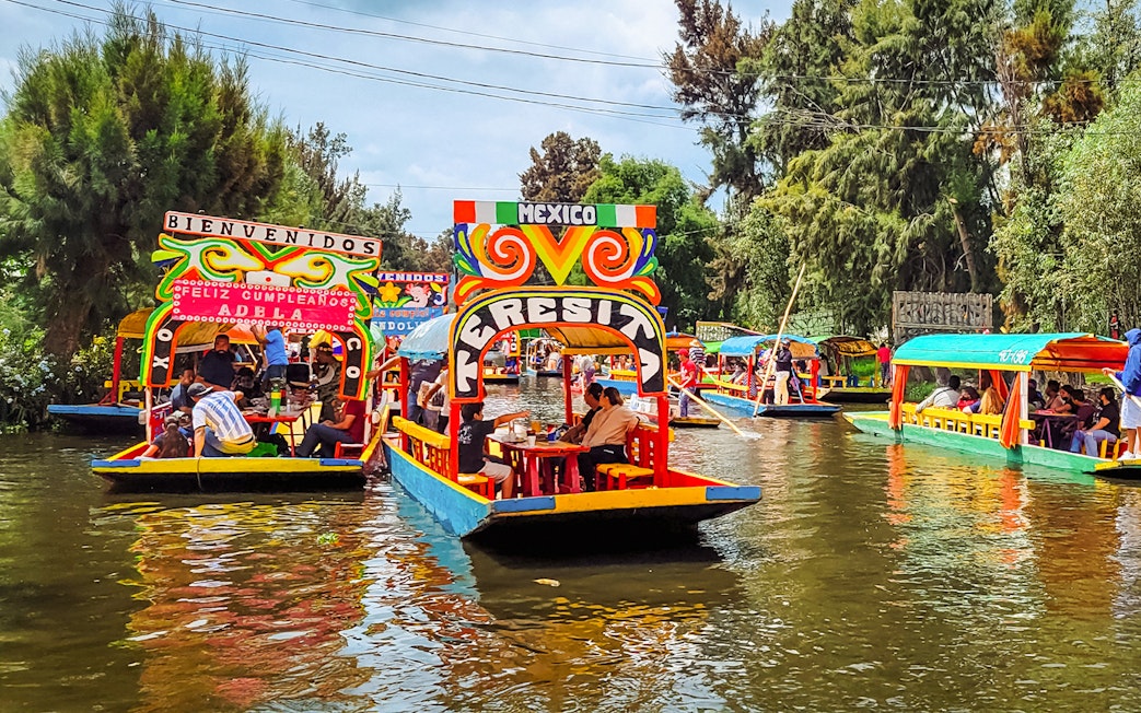 Colorful trajineras on Xochimilco canals, Mexico, with people enjoying a boat tour.