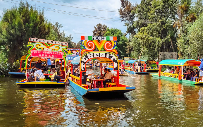 Colorful trajineras on Xochimilco canals, Mexico, with people enjoying a boat tour.