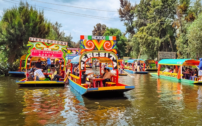 Colorful trajineras on Xochimilco canals, Mexico, with people enjoying a boat tour.