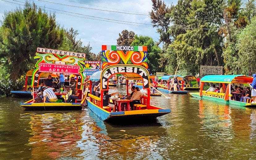 Colorful trajineras on Xochimilco canals, Mexico, with people enjoying a boat tour.