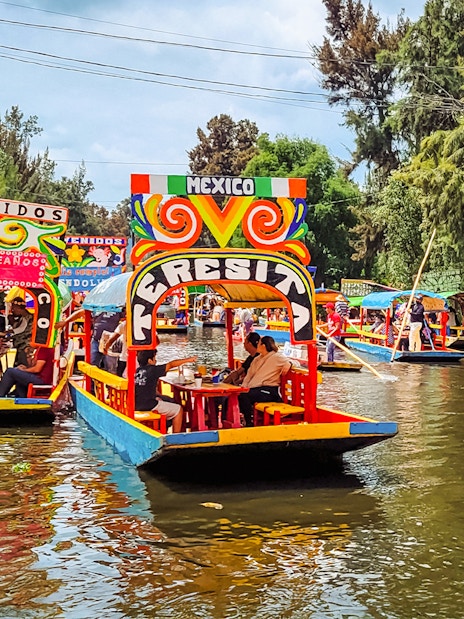 Colorful trajineras on Xochimilco canals, Mexico, with people enjoying a boat tour.