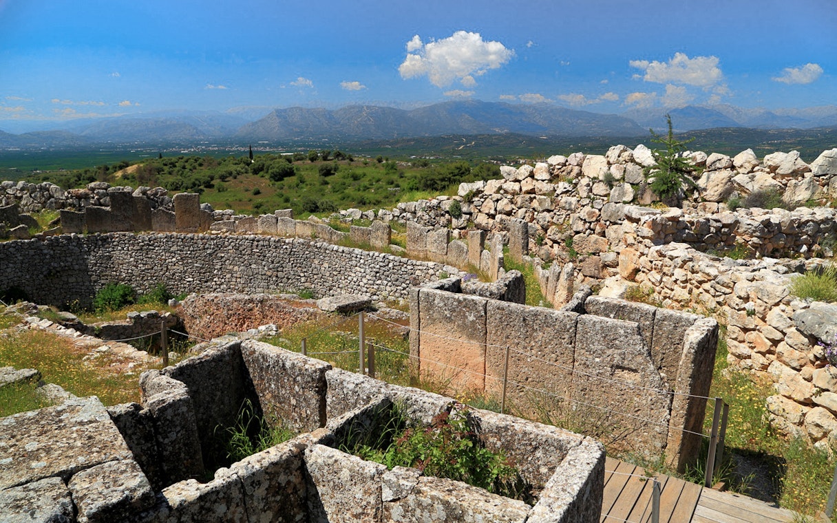 Mycenae archaeological site with ancient stone walls and distant mountain view.