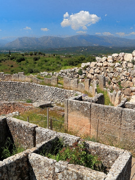 Mycenae archaeological site with ancient stone walls and distant mountain view.