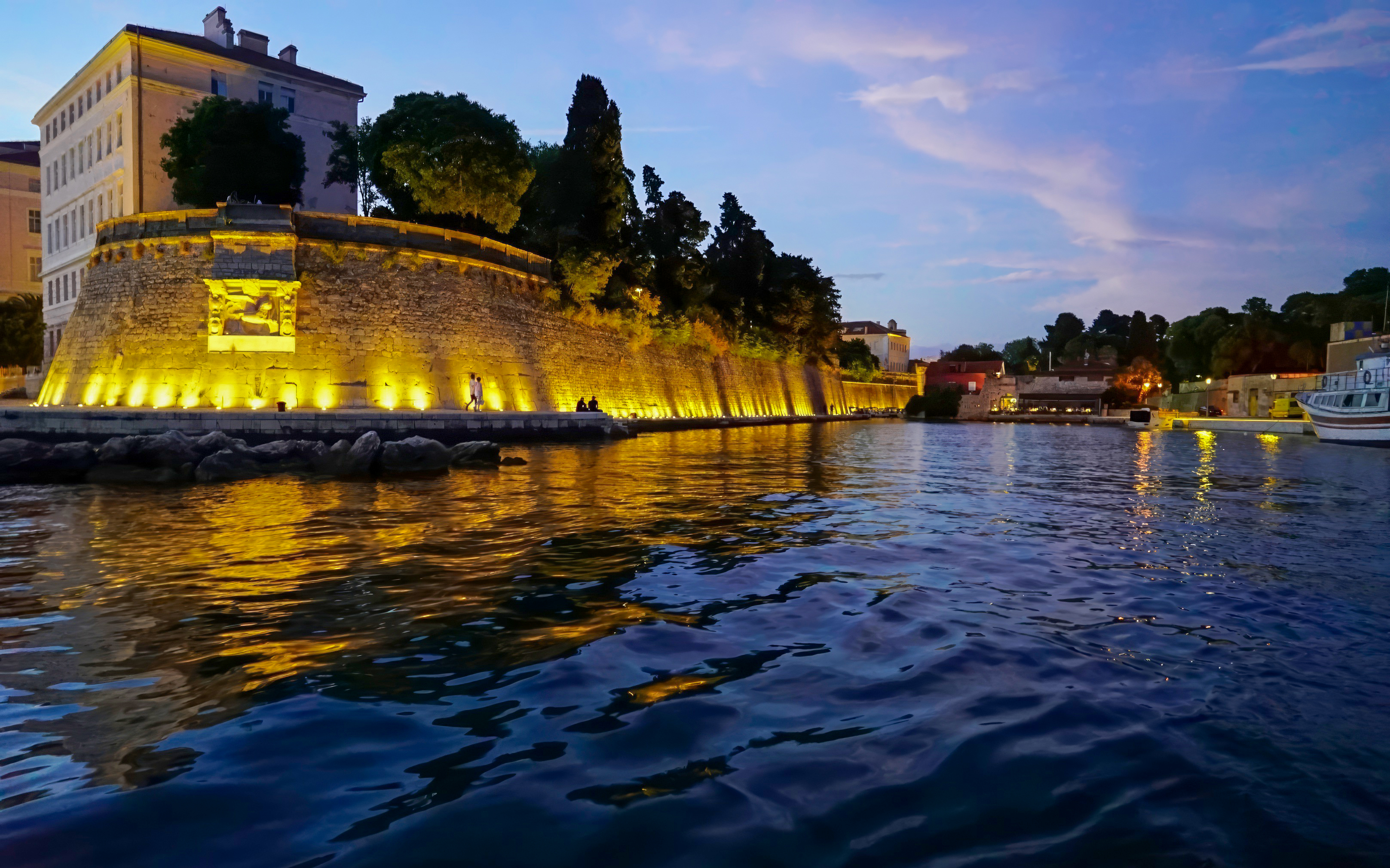 Zadar waterfront at sunset with illuminated city walls and calm sea.