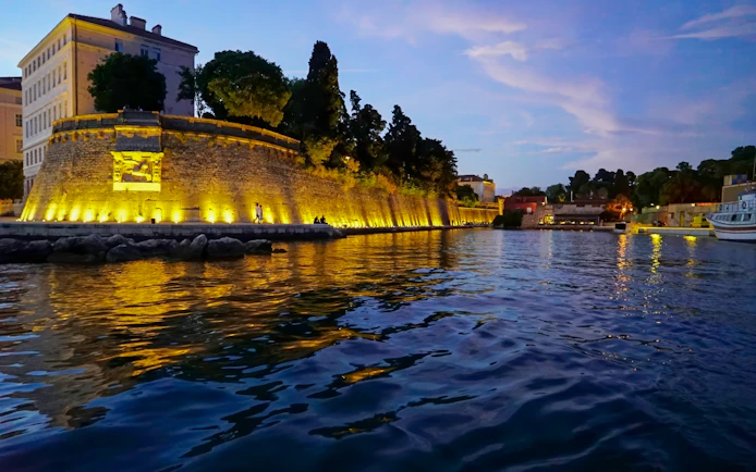 Zadar waterfront at sunset with illuminated city walls and calm sea.