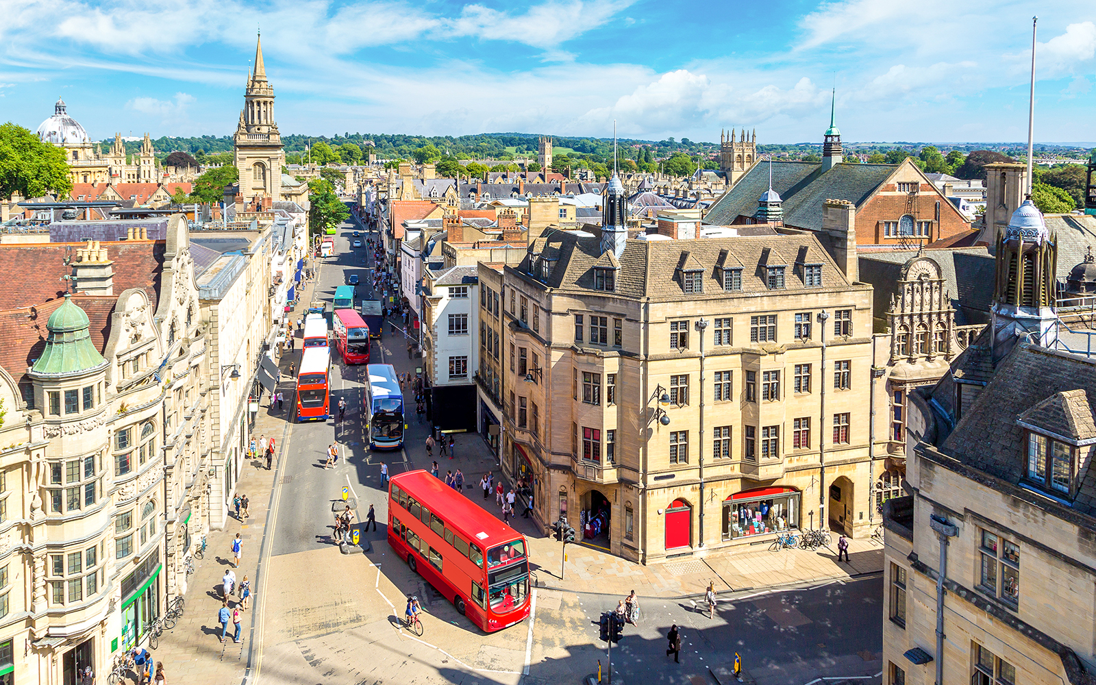 Buses on a busy street in Oxford, with historic buildings and spires in the background.