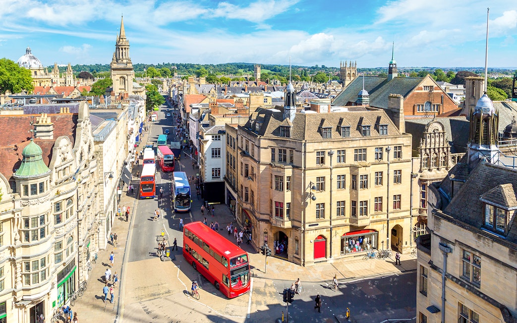 Buses on a busy street in Oxford, with historic buildings and spires in the background.