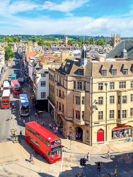 Buses on a busy street in Oxford, with historic buildings and spires in the background.