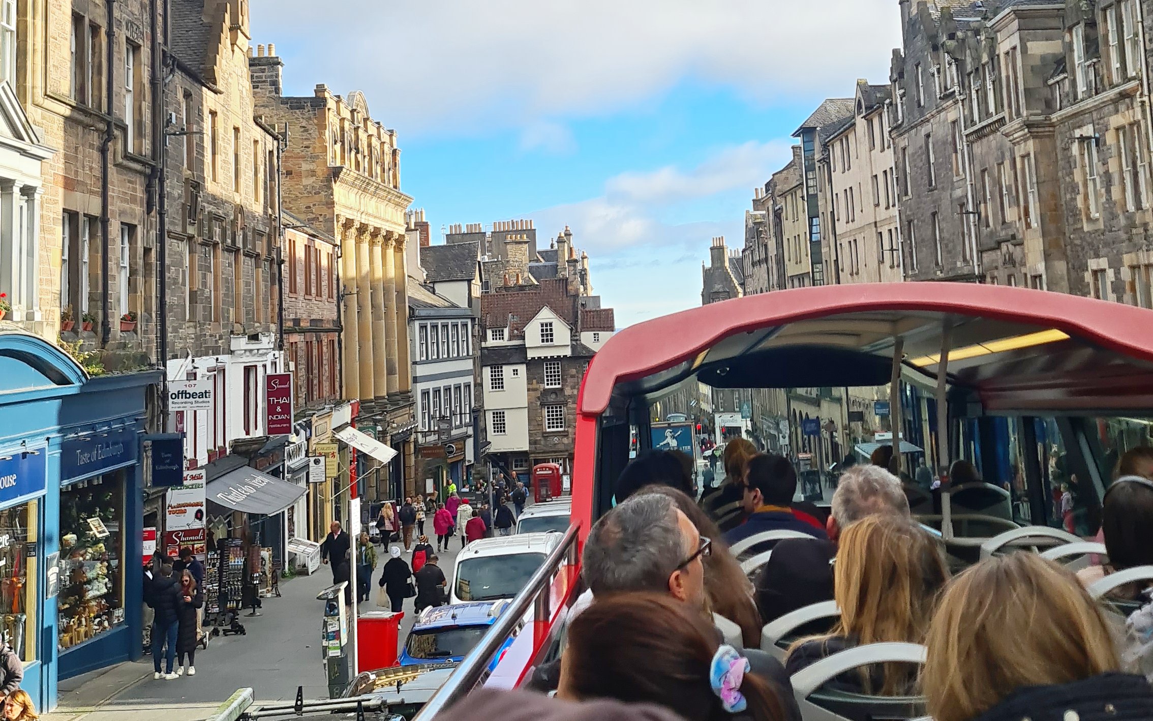 Open-top bus tour on Edinburgh's historic street with stone buildings.