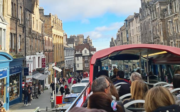 Open-top bus tour on Edinburgh's historic street with stone buildings.