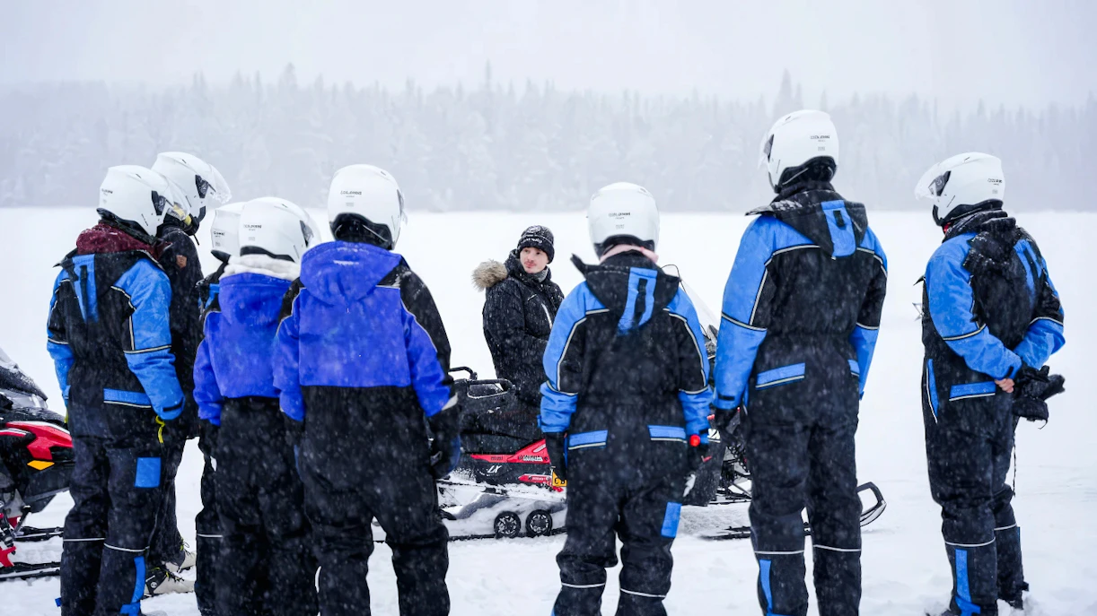 Group preparing for Arctic snowmobile safari in snowy Rovaniemi landscape.