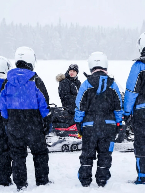 Group preparing for Arctic snowmobile safari in snowy Rovaniemi landscape.