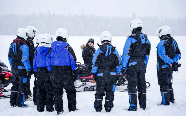 Group preparing for Arctic snowmobile safari in snowy Rovaniemi landscape.
