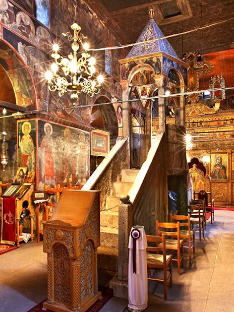 Interior of Varlaam Monastery with frescoes and ornate wooden iconostasis.