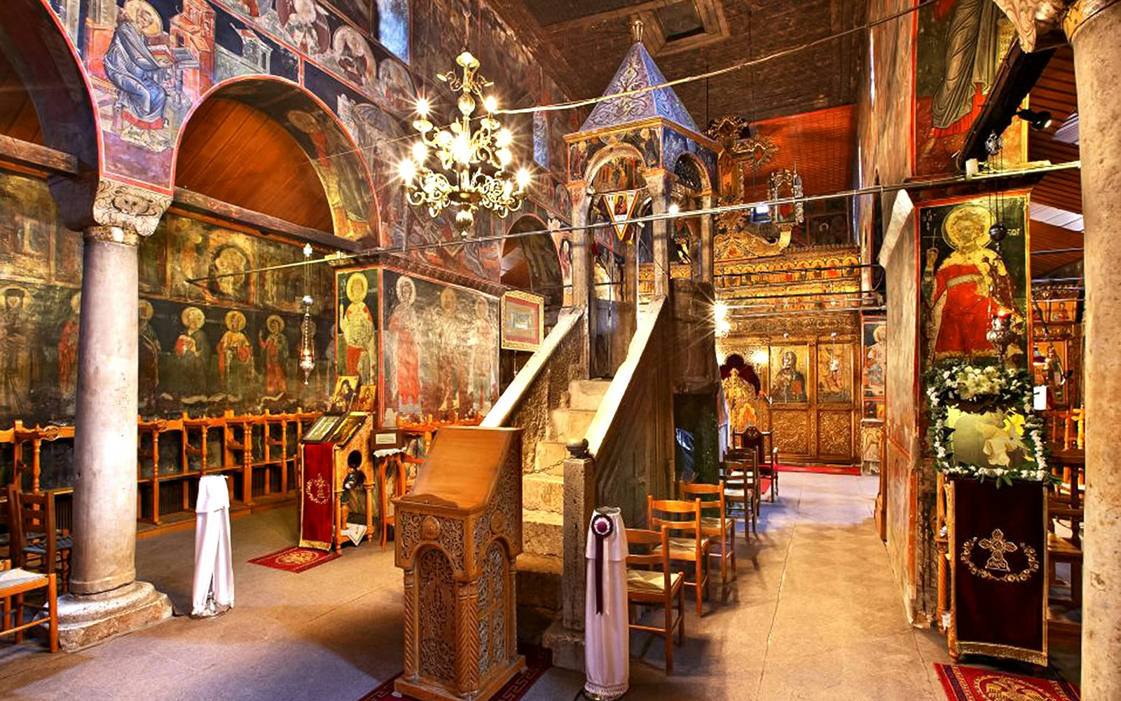 Interior of Varlaam Monastery with frescoes and ornate wooden iconostasis.