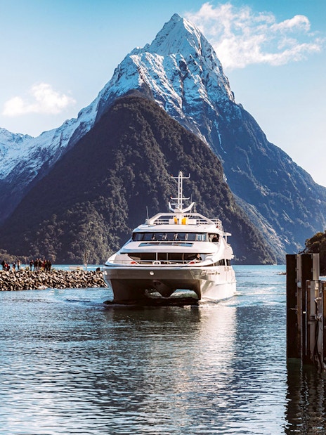 Cruise boat in Milford Sound with fjord views, lush mountains, and waterfalls, New Zealand.