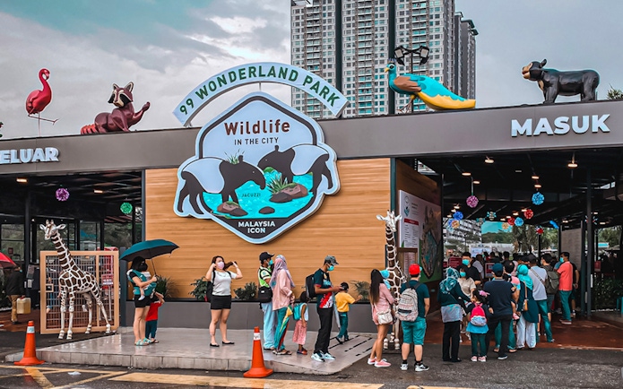 Visitors queue at the entrance of 99 Wonderland Park, Kuala Lumpur, with animal sculptures above.