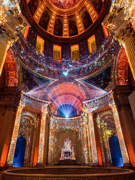 Immersive light display inside Invalides, Paris, showcasing vibrant projections on columns and ceiling.