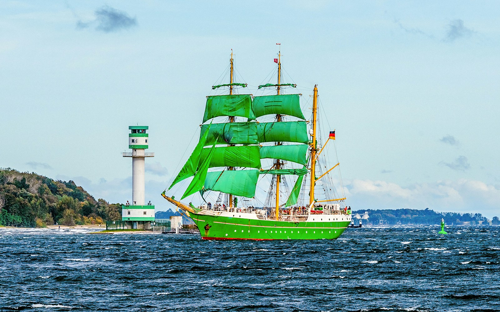 Alexander von Humboldt II ship sailing near a coastal city with green sails visible.