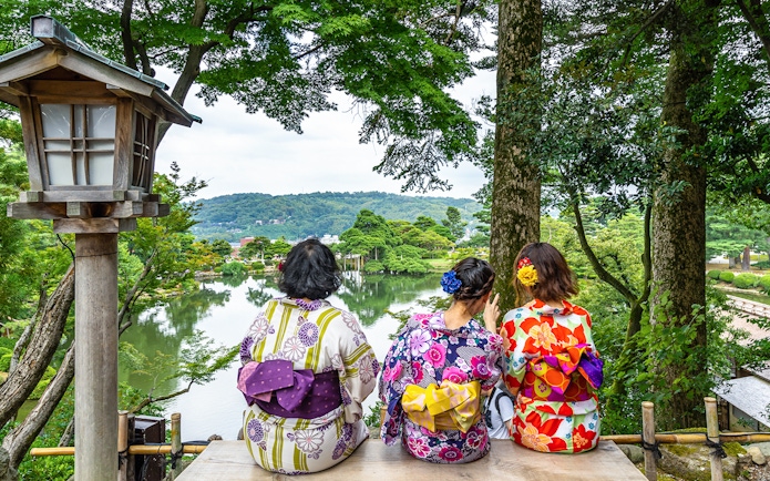 Three people in traditional kimonos overlooking Kenrokuen Garden in Kanazawa, Japan.