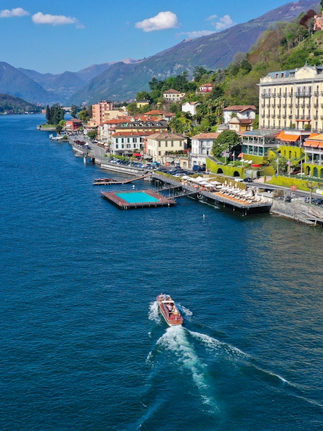 Aerial view of Lake Como with a boat near the shoreline and mountains in Lombardy, Italy.