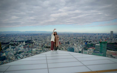 Visitors taking a selfie on Shibuya Sky observation deck with Tokyo cityscape in the background.