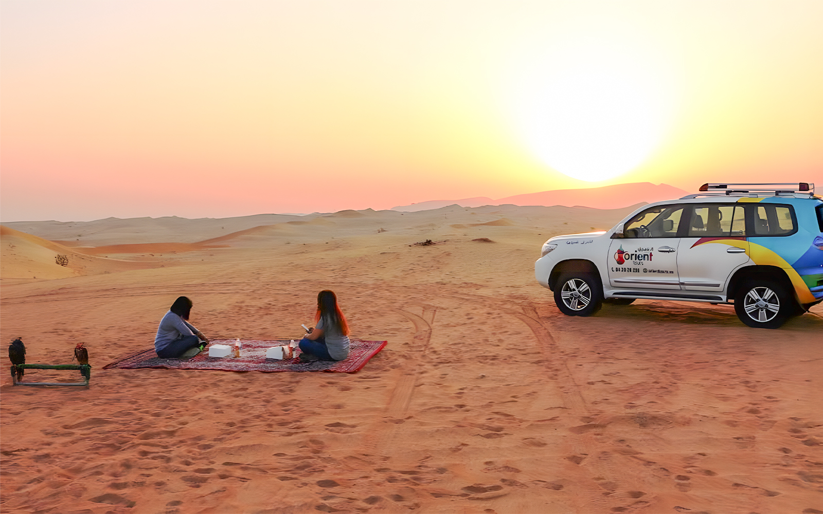 People enjoying sunrise in Abu Dhabi desert with SUV nearby.