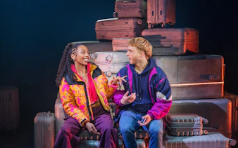 Two actors conversing on stage with suitcases in "Two Strangers" Broadway show.