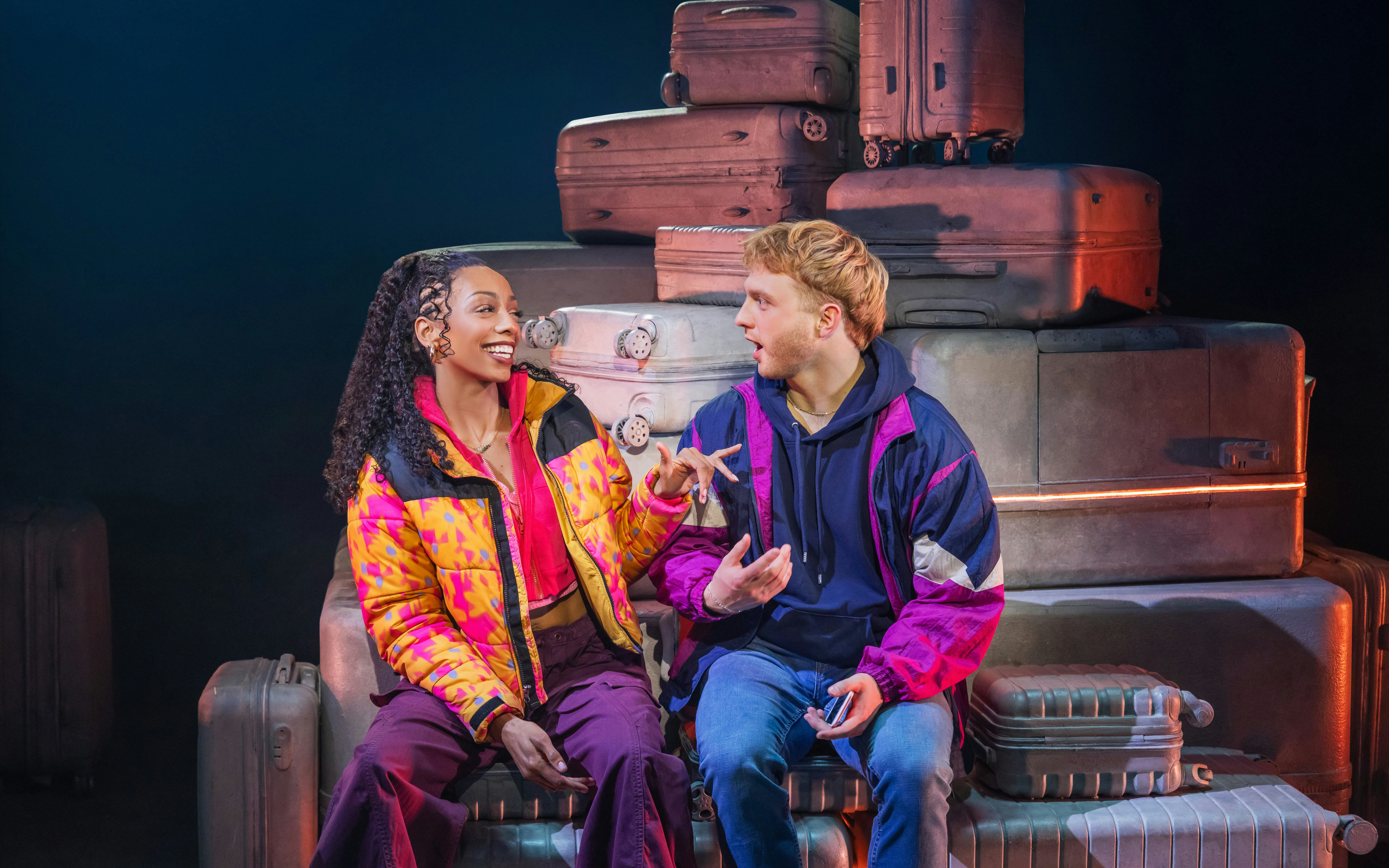 Two actors conversing on stage with suitcases in "Two Strangers" Broadway show.