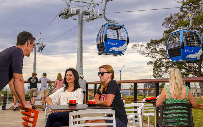 People enjoying coffee on a deck with Arthurs Seat Eagle gondola in the background.