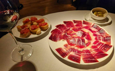 Cured ham, tomato-topped bread, olives, and wine on a table in Valencia cooking class.