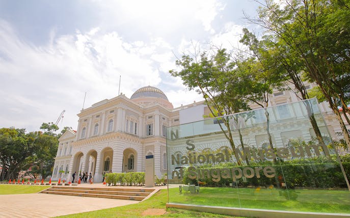 National Museum of Singapore exterior with glass sign and trees.