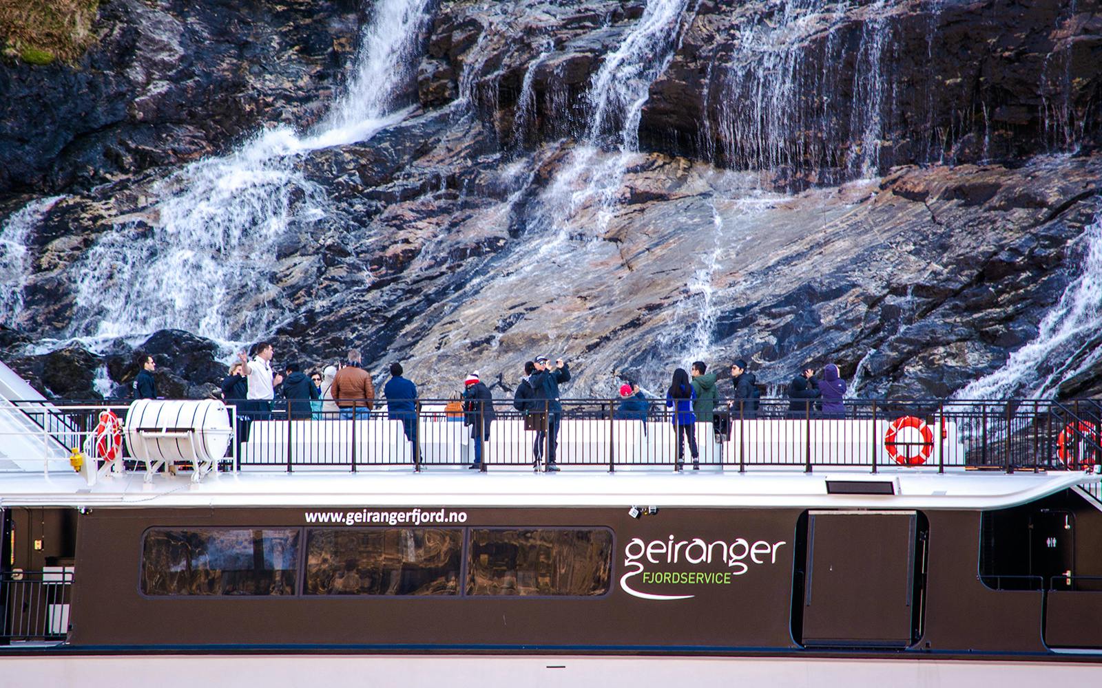 Guests on a fjord cruise in Alesund, Norway, viewing a waterfall.