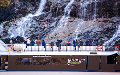 Guests on a fjord cruise in Alesund, Norway, viewing a waterfall.