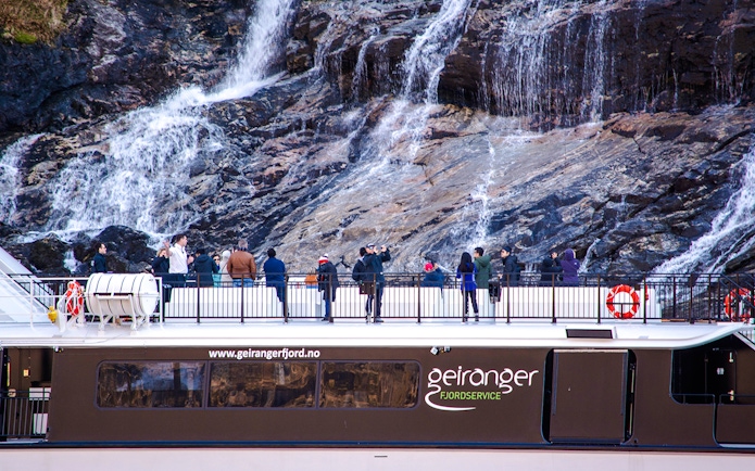 Guests on a fjord cruise in Alesund, Norway, viewing a waterfall.