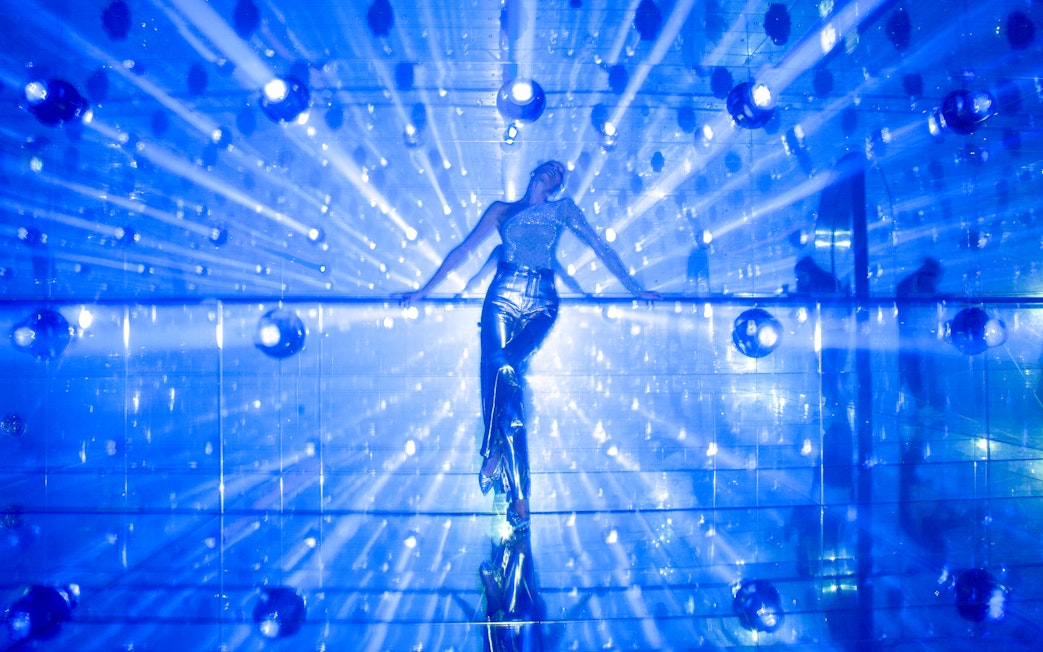 Person in reflective outfit at Harmonia zone, AYA Universe, Dubai with blue light beams.