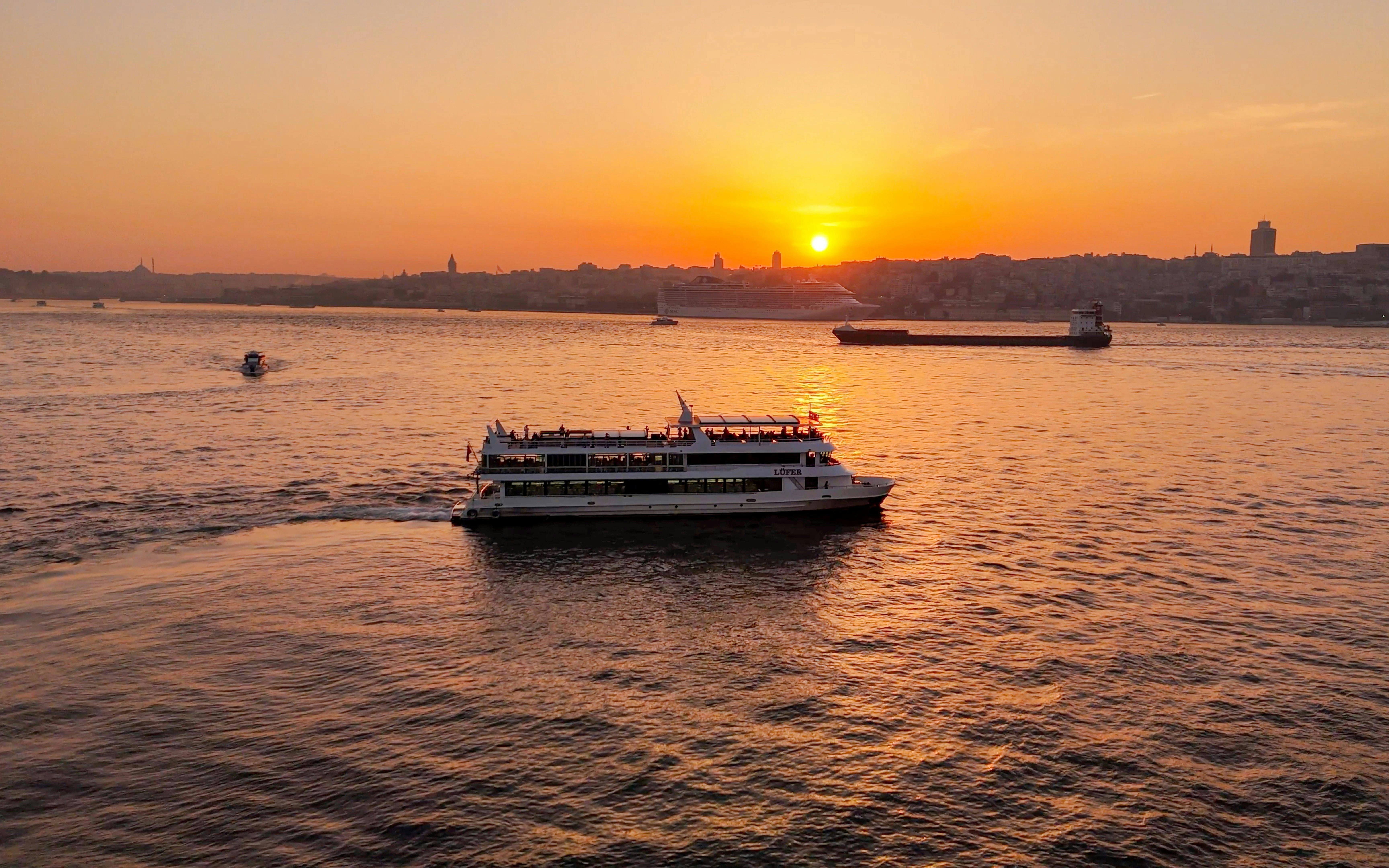 Sightseeing cruise on Bosphorus Strait at sunset with city skyline in background.