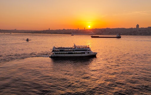 Sightseeing cruise on Bosphorus Strait at sunset with city skyline in background.