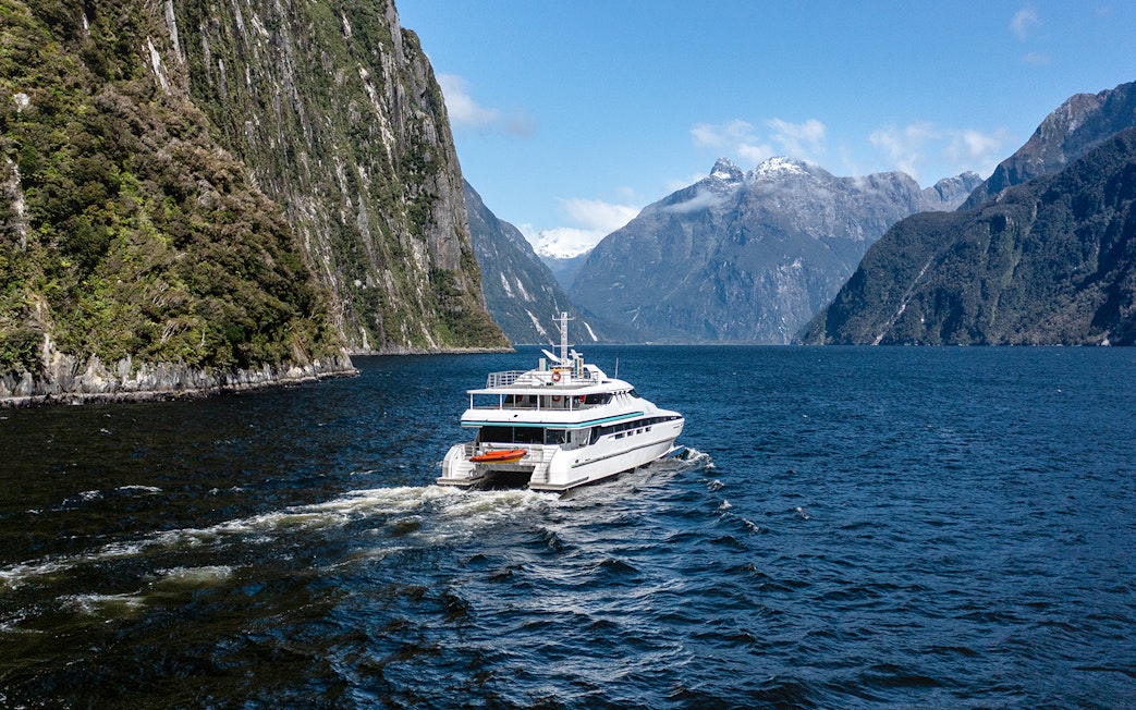 Cruise ship sailing through Milford Sound with mountain views.