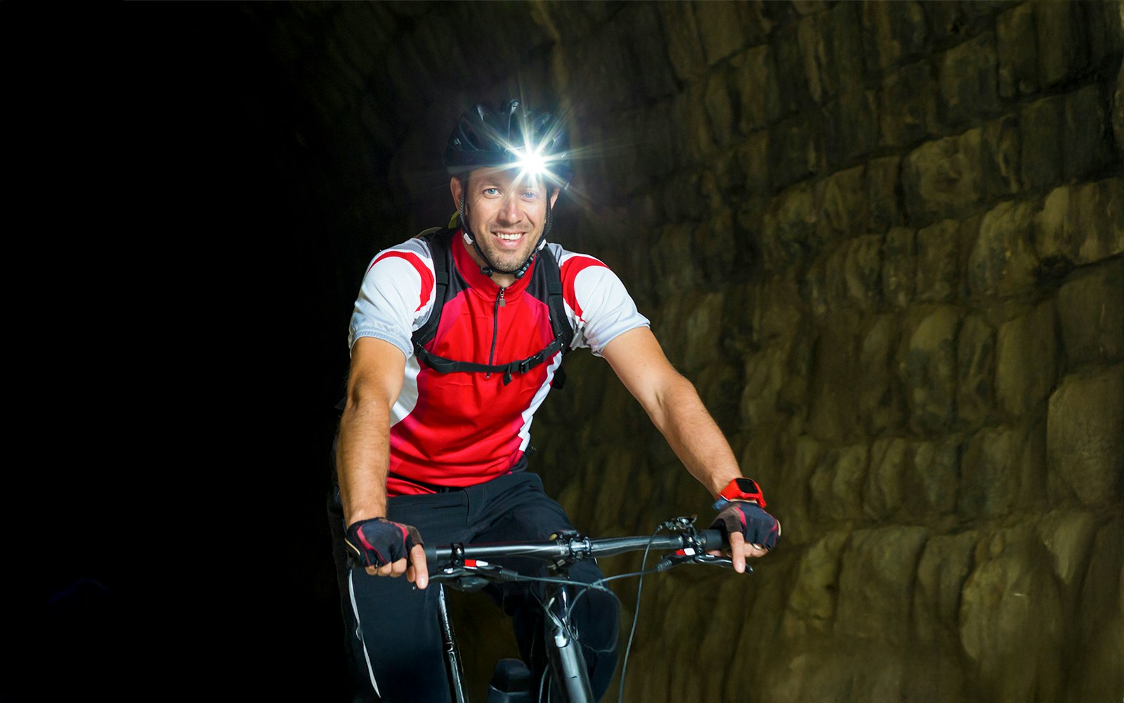 Man cycling in a tunnel with helmet light and safety gear.